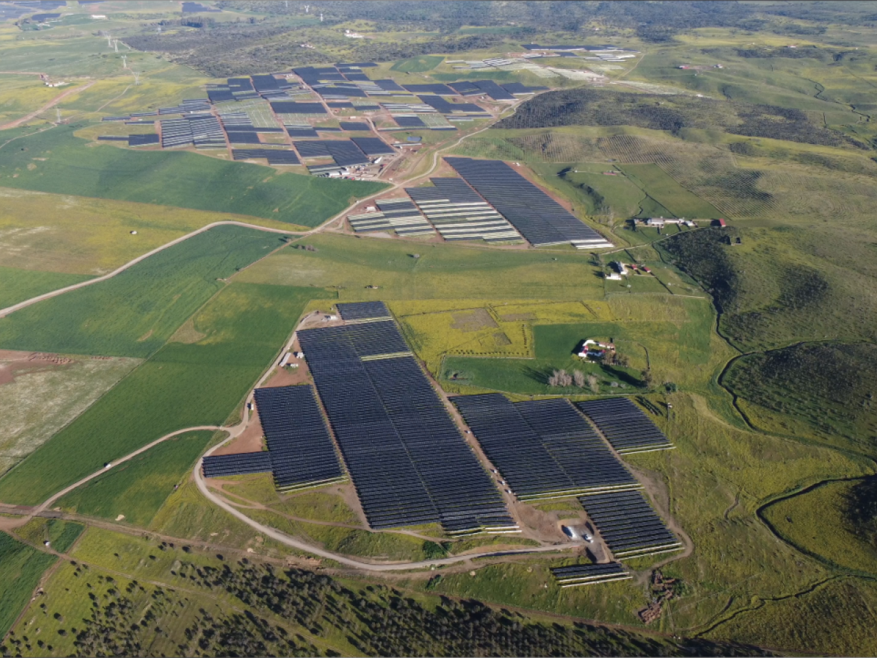 Aerial panoramic view of green fields, solar panels covering parts.