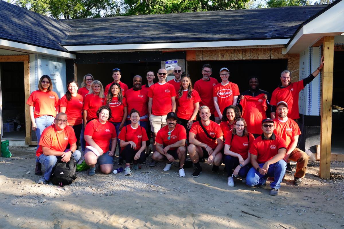 Group of people in red shirts posing in front of home being built