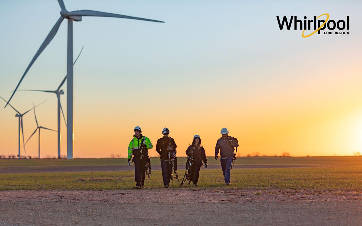 four workers in safety gear walking in front of wind turbines at dawn
