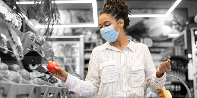 a person holds a red apple in a grocery store, a basket in their other hand
