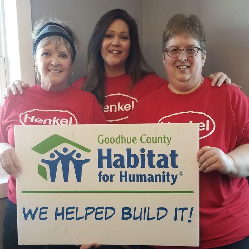 Three volunteers holding a sign "Habitat for Humanity Goodhue County. We helped build it!"
