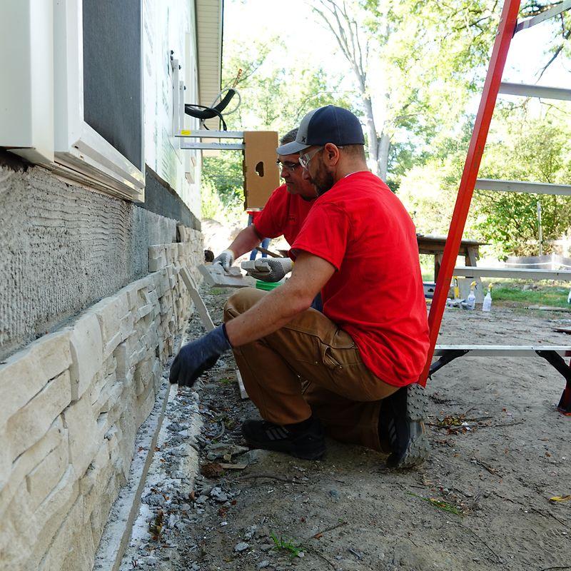 Two volunteers putting rock siding on the base of a house