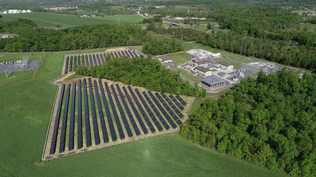 Field of solar panels next to a campus of building in a forested area