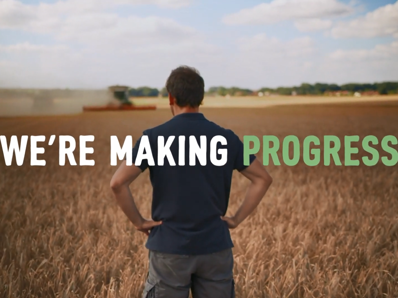 "We're Making Progress" over a person, with hands on hips, looking out over a crop field.