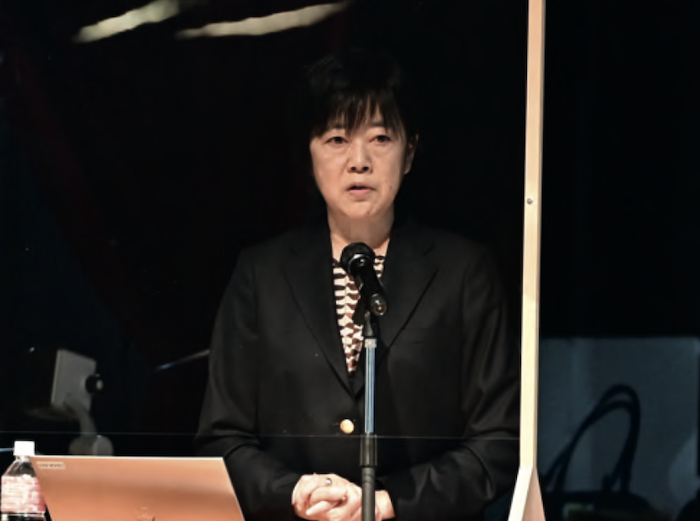 Japanese Aflac employee speaking at a podium.
