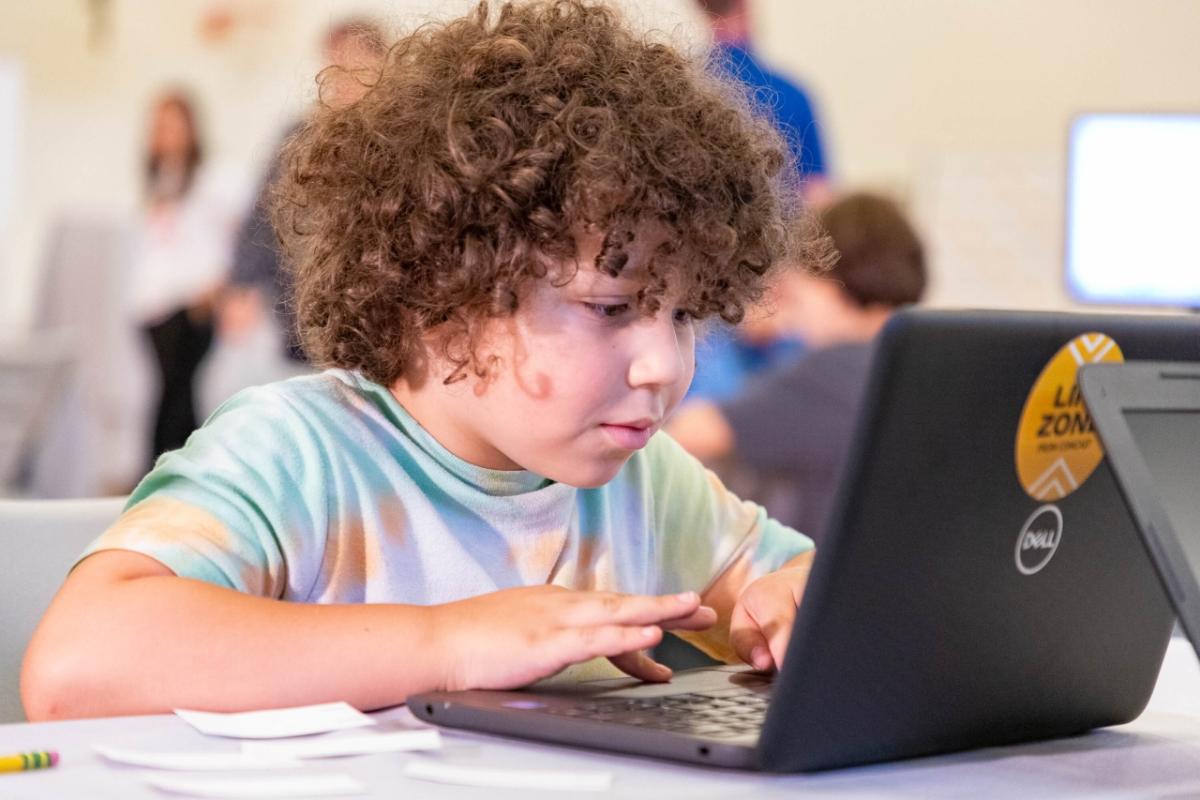 a child engaged on a laptop, others blurred behind him