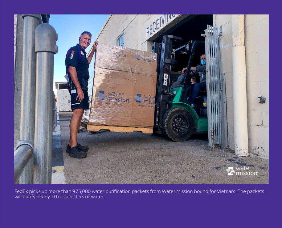 FedEx employee standing by forklift with large boxes labeled Water Mission. Caption reads "FedEx picks up more than 975,000 water purification packets from Water Mission bound for Vietnam. The packets will purify nearly 10 million liters of water.