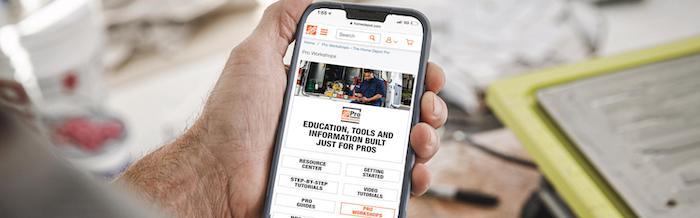 Smartphone being held in a hand; showing the Home Depot Pro Workshops app.
