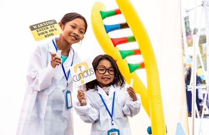 Two young female students shown in lab coats and a double helix.