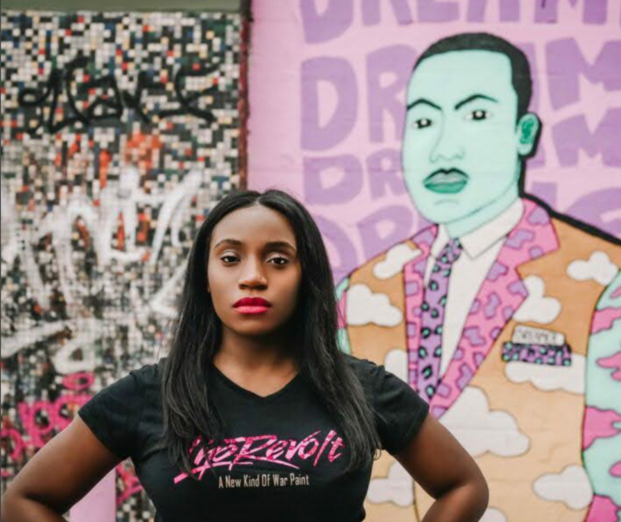 Courtney Wright wearing a "LipRevolt" tshirt in front of a mural of Martin Luther King