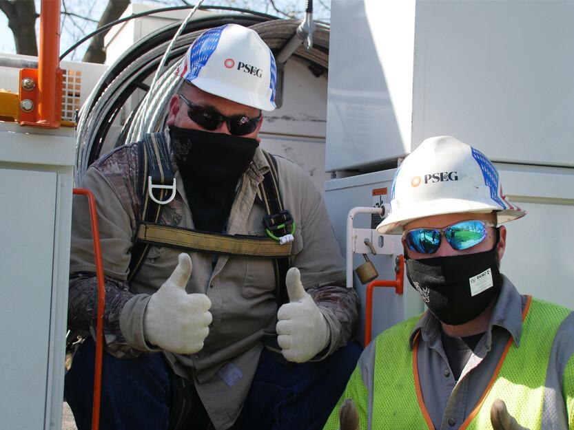 Two PSEG technicians; wearing helmets and masks giving the thumbs up sign.