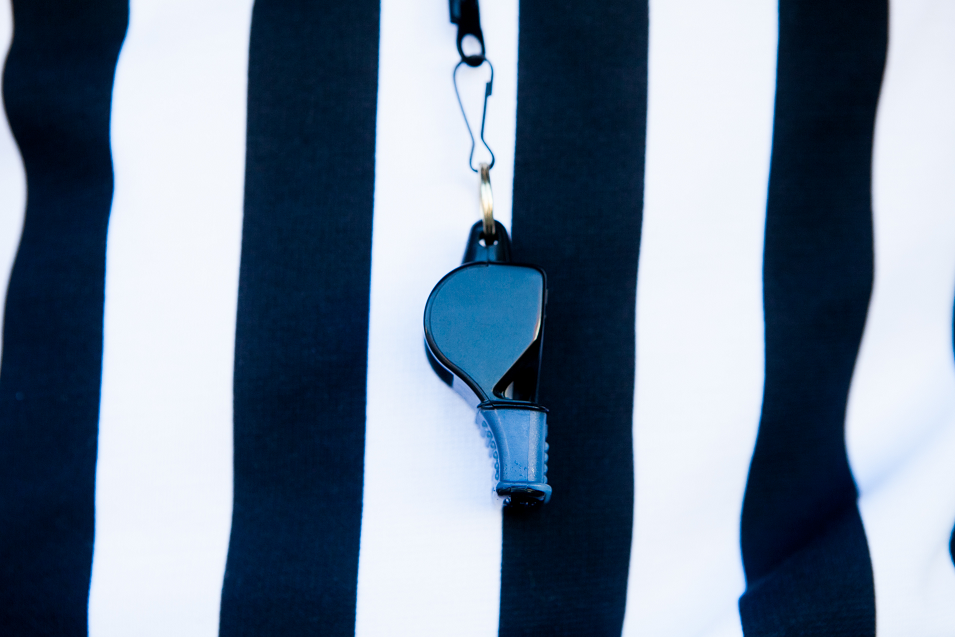close up of black and white stripped referee shirt with blue whistle