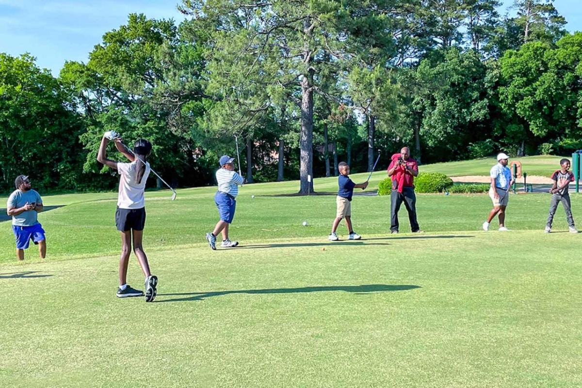 Black students practice their golf swings on a rolling green field