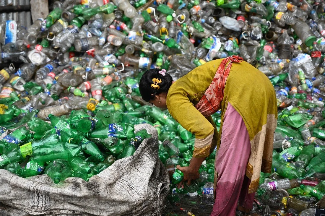 Woman in front of large pile of plastic bottles