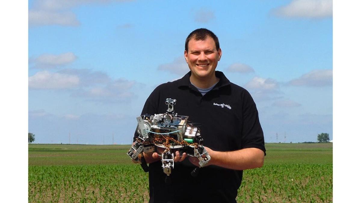 David Dorhout holds a robot while standing in a field
