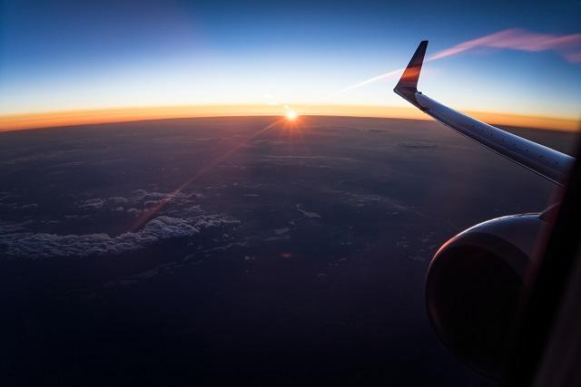 passenger view of the wing of a plane, the sun setting in the horizon