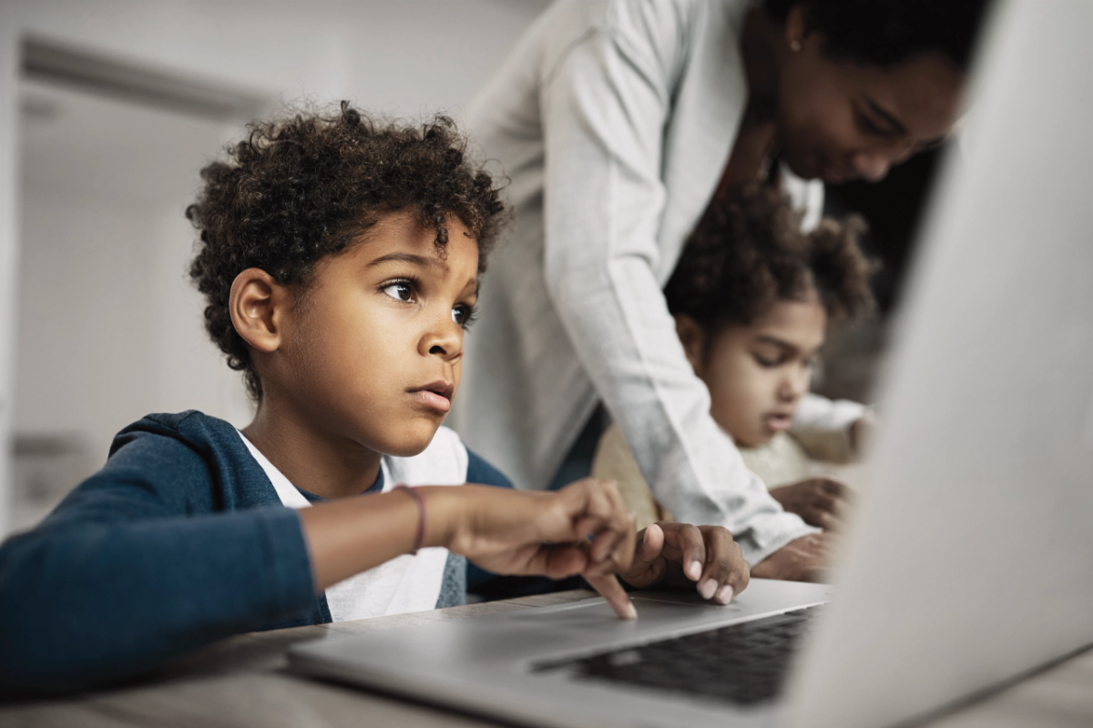 A child using a laptop next to another child on a laptop with an adult assisting them