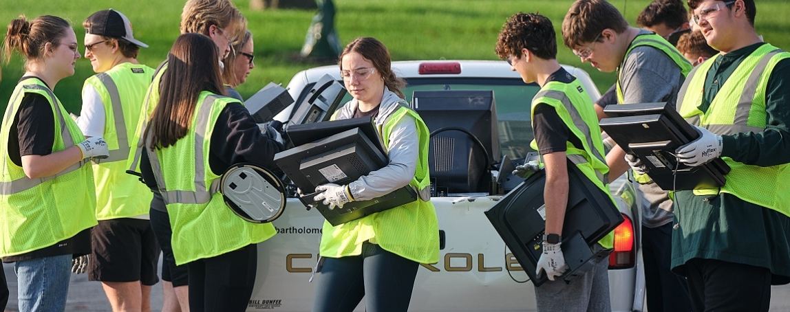 A group of people with safety vests, gloves, and glasses unload electronics from the back of a truck.