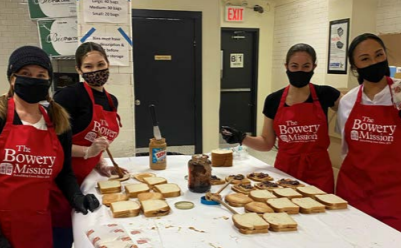 a group of four people wearing "the bowery mission" aprons, making lots of sandwiches