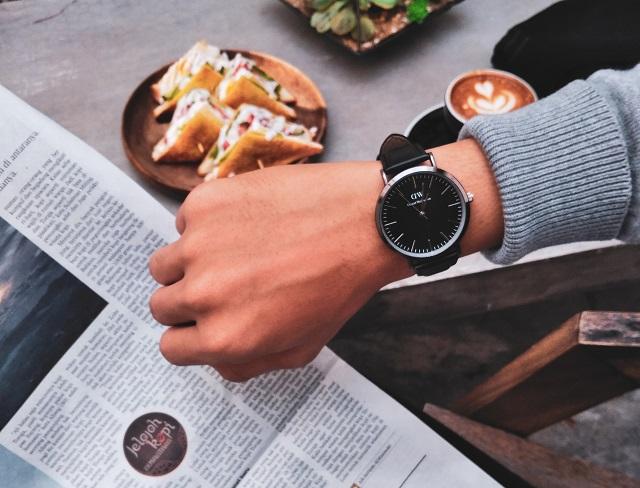 a hand with a watch, a newspaper and food on the table