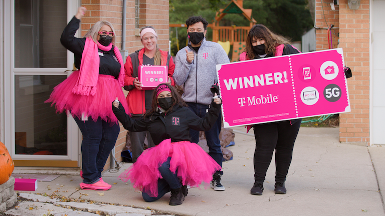 group of people, some wearing pink tutus, one holding a large sign "Winner! T-Mobile"