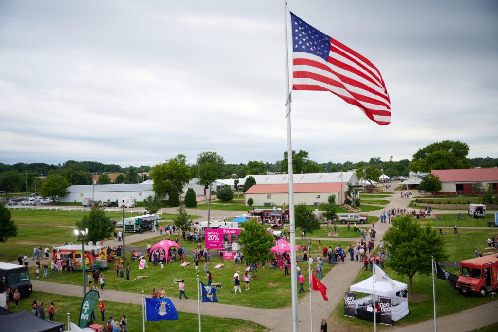 aerial view of a campground, an American flag on a tall pole, vendor booth tents and out buildings on the grounds.