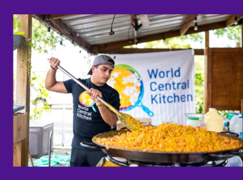 Volunteer cooking a big pot of food with a World Central Kitchen sign behind him 